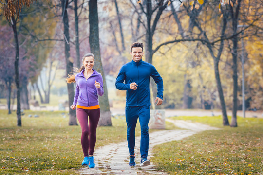 女人和男人在秋天公园的小路上跑步运动
