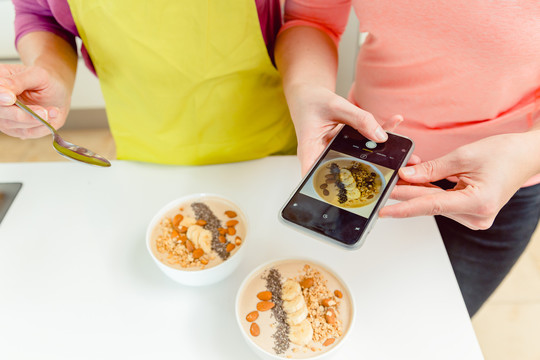 女性美食博主通过手机为博客拍摄健康燕麦碗的照片