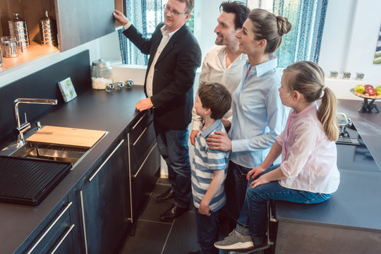 一家人带着孩子在展厅的厨房里看着，想用现代的厨房来代替他们的旧厨房