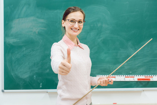 课堂上友好的老师站在黑板前，手里拿着一个指针
