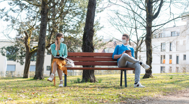 戴着面具的女人和男人坐在公园的长椅上进行社交距离调情