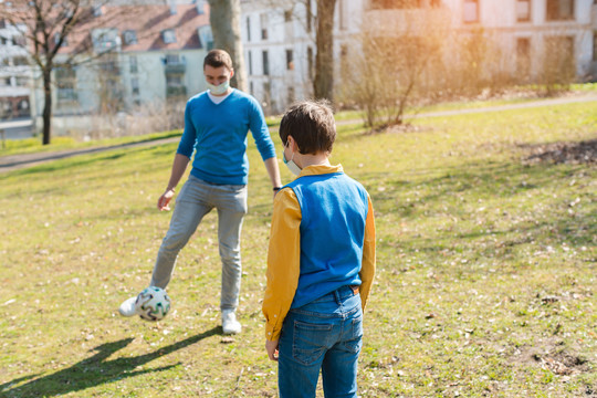 天气晴朗，冠状病毒危机期间，爸爸和儿子在公园里踢足球