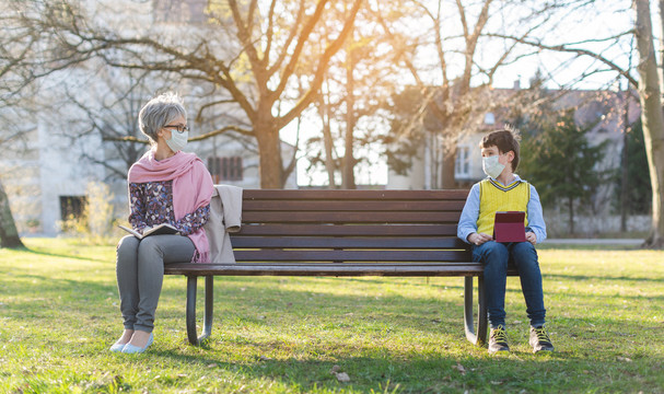 祖母和孙子在公园长椅上因社交距离而分开