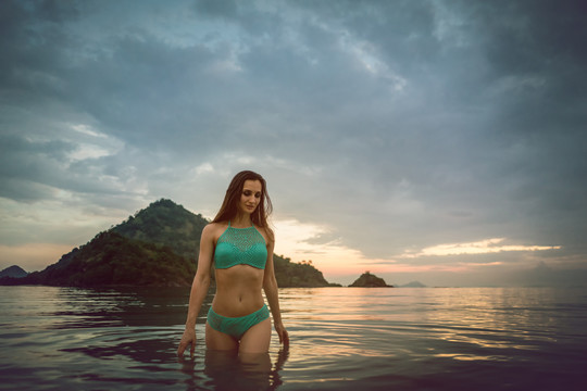 在海滩度假时，日落时在热带海洋中沐浴的女人