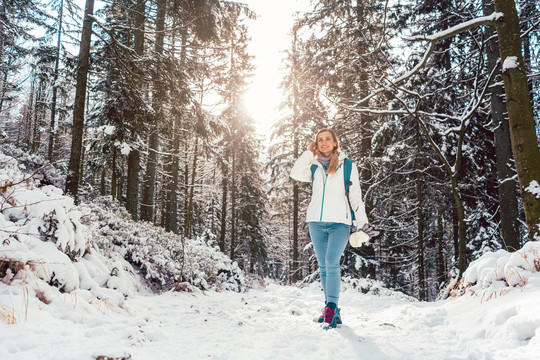 站在寒冷的雪地里，沿着穿过树林的小路徒步旅行的女人