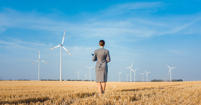 绿色能源的投资者看着她穿着西装站在地上的风力涡轮机
