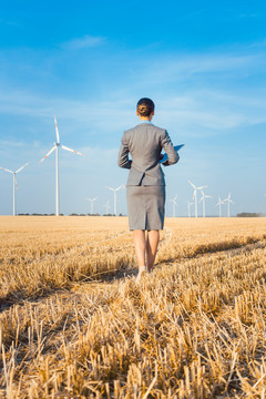 绿色能源的投资者看着她穿着西装站在地上的风力涡轮机