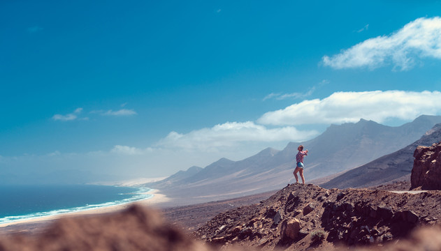 站在火山岩上的女人惊叹于富尔特文图拉海岸，欣赏着广阔的风景