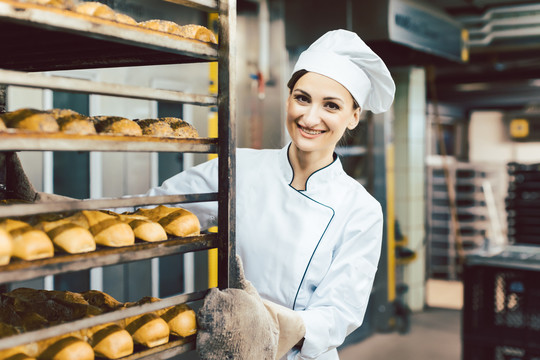 面包师妇女戴面包师手套在烤箱里推着面包单