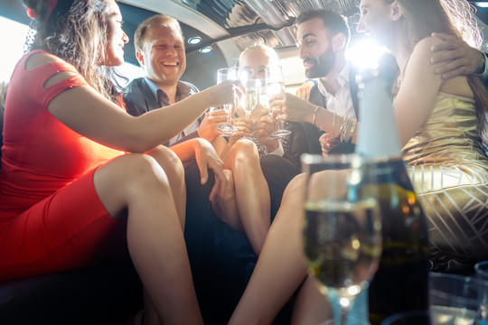 一群聚会的人坐在一辆豪华轿车里，喝着酒，男人和女人在玩