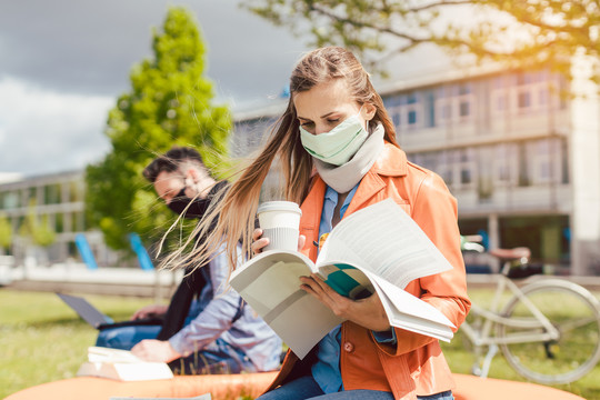 大学校园里的一名女学生在使用笔记本电脑时正在学习戴口罩