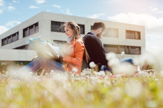 一男一女学生坐在大学校园的草地上看书