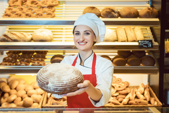 在面包店，一名女售货员拿着围裙，向镜头展示新鲜面包
