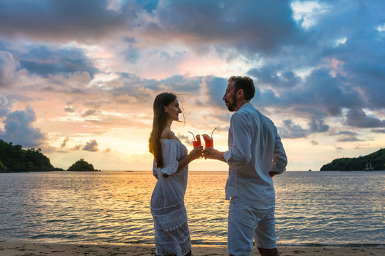 热带度假的情侣们在五颜六色的日落时分，在海边的海滩上举杯祝酒