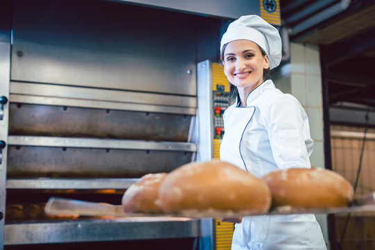 面包师妇女在铁锹上展示刚烤好的面包，几乎可以闻到新鲜的味道