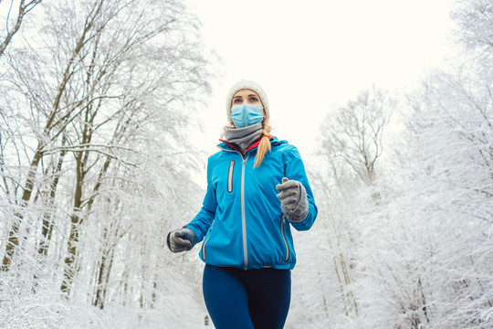 雪地景观中2019冠状病毒疾病的女性跑步或戴面罩慢跑