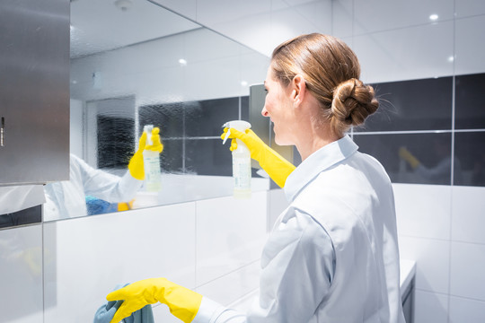 女清洁工或清洁工在洗手间清洁镜子