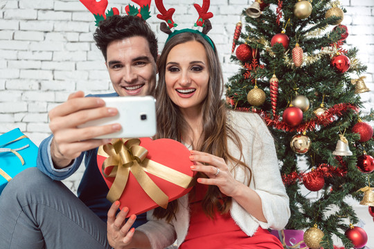 情侣们在圣诞节用手机拍自拍照片，以便在社交媒体上分享