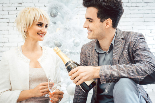 女人和男人在白色圣诞树下，喝着起泡酒，享受着节日的快乐