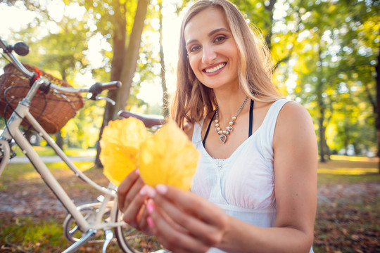 一位妇女停下自行车，收集美丽的秋叶，看着它们