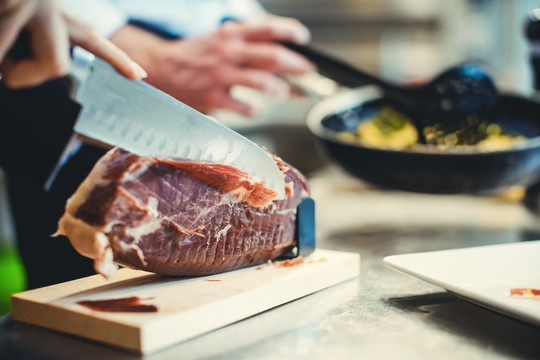 厨师用刀切帕尔玛火腿以备烹饪时使用的详细照片
