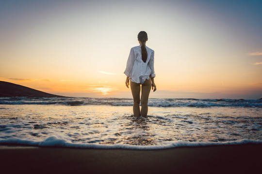 在忧郁的日落中，一个女人站在海滩上，站在水中