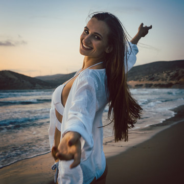 日落时分，一个在海滩上玩得很开心的女人张开双臂