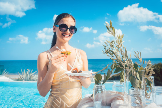 身着金色连衣裙的女子在以泳池和海滩为背景的海滩派对上吃东西