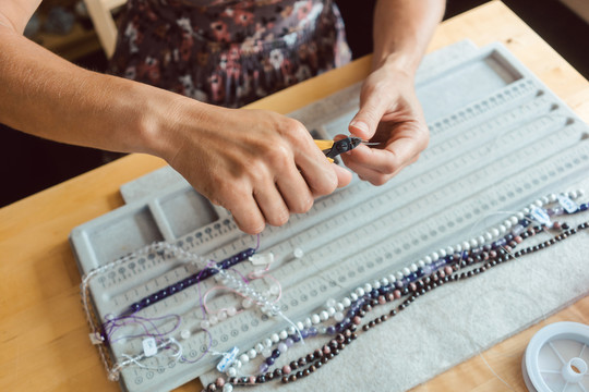 特写镜头：一个女人用宝石做项链，把它们串在绳子上