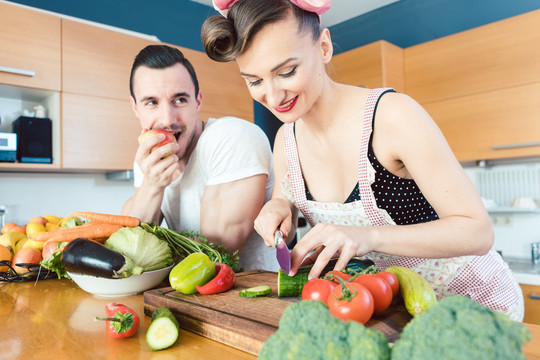 一个相当懒的男人一边吃苹果一边看着他的妻子准备食物