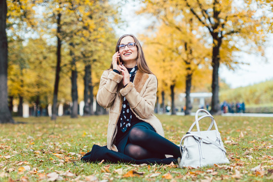 秋天坐在草地上用手机给朋友打电话的女人
