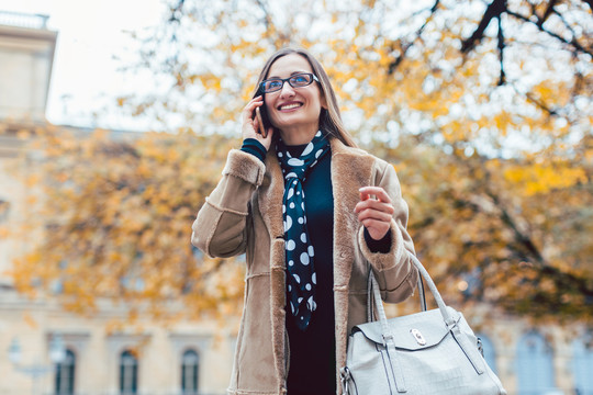 秋天，美丽的女人站在城市里用她的手机