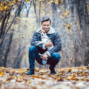 一个年轻人牵着他的狗在秋天的公园里散步，依偎着宠物