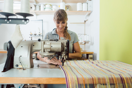 裁缝店的女裁缝在缝纫机上缝制彩色装饰织物