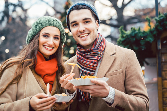 在圣诞集市上吃零食的男人和女人看起来很开心