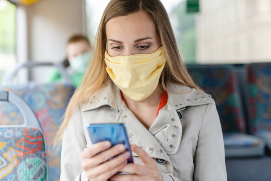 在公共汽车上使用电话的妇女戴着口罩，因为我们仍然有流行病