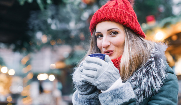 冬市上的圣诞树前喝着热酒的女人看着相机