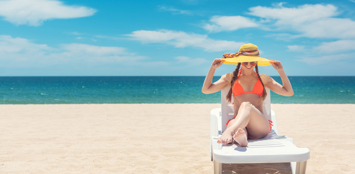 一名妇女举着帽子在海边的海滩上晒太阳