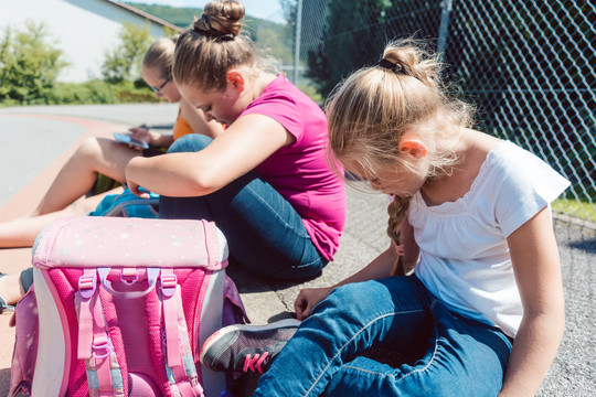 三个女孩坐在学校前面的人行道上等公共汽车