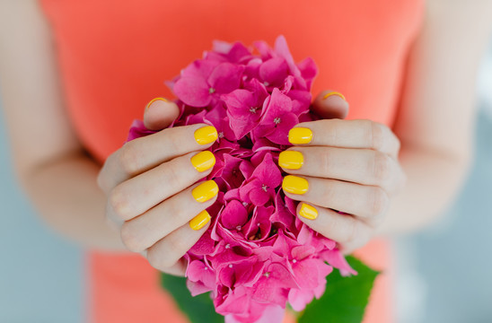 修剪过黄色指甲的妇女手里拿着一朵花