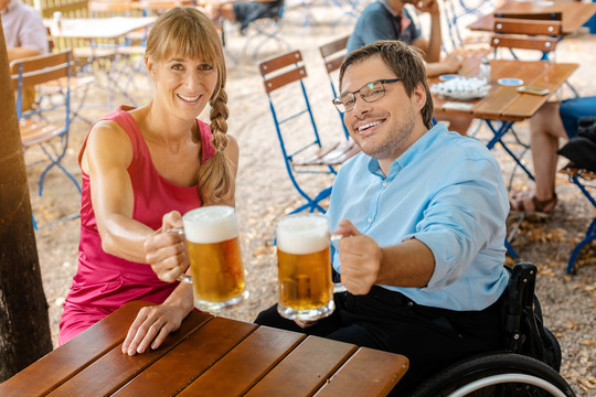 坐在轮椅上的残疾人和喝啤酒碰杯的朋友