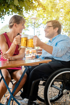 坐在轮椅上的残疾人和喝啤酒碰杯的朋友