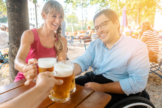 朋友们在啤酒园喝酒，一个人坐在轮椅上，所有人都在碰杯