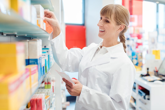 微笑的药剂师或化学家在药房的货架上分类药物的妇女