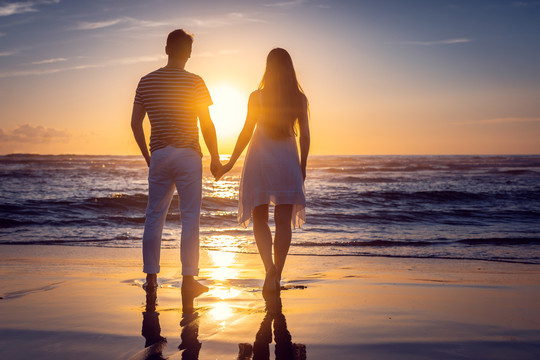 一对浪漫的情侣手牵着手站在海边的海滩上度假