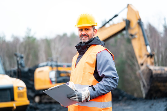 一名采石工人站在挖掘机前微笑的画像