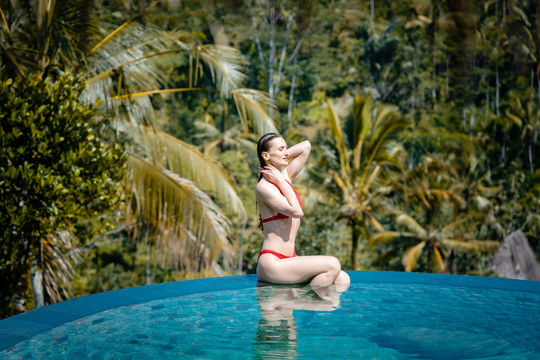 热带度假的女人坐在棕榈树前的水池里