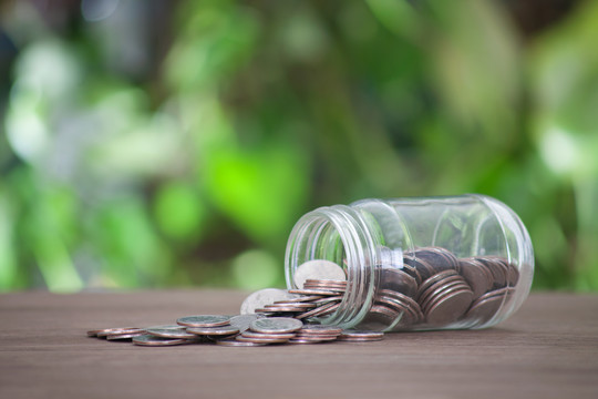 桌子上倾倒的玻璃瓶散落美元硬币