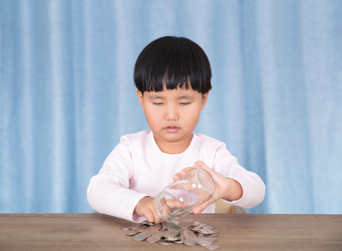 小女孩在玩耍玻璃瓶里的美元硬币