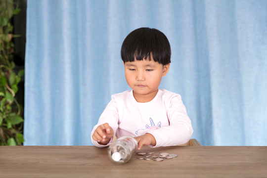 小女孩在玩耍玻璃瓶里的美元硬币